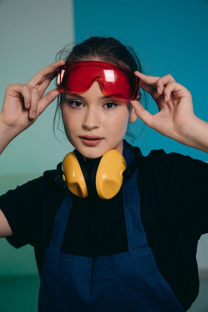Portrait of a young woman wearing protective goggles and headphones in a workshop.